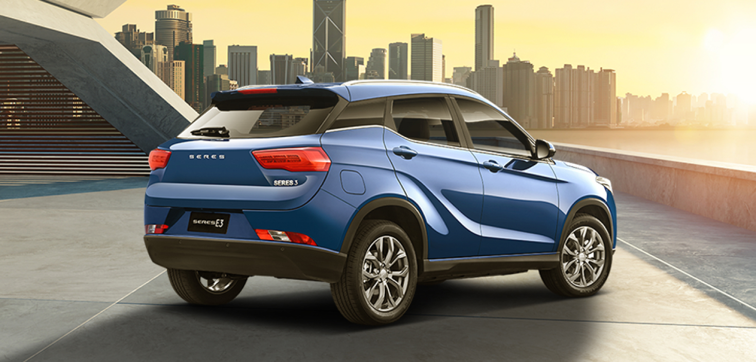 Vista trasera de Auto electrico Seres 3 color azul estacionado con edificios y atardecer de fondo